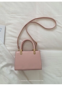 Vue à plat d'un sac à main rose pâle en cuir avec des garnitures dorées sur tissu