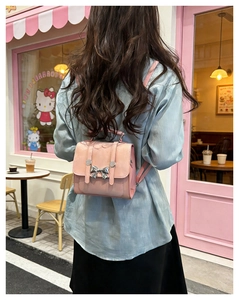 Rear view of a pink mini faux leather backpack with a bow buckle in a street cafe setting