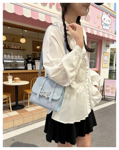 Close-up of a light blue faux leather crossbody bag with a silver bow metal decoration