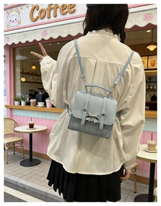 Close-up of light blue mini backpack with silver butterfly detail in a cafe setting