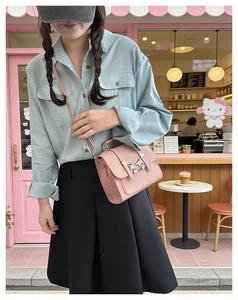 Pink crossbody bag with silver butterfly detail worn by a model in a trendy cafe setting
