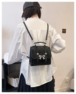 Detail of a black leather mini backpack featuring a silver bow buckle and studded flap