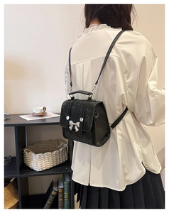 Detail of black matte mini backpack with silver bow buckle worn by model on shoulder