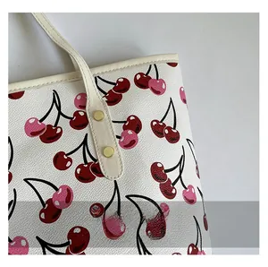 Close-up of cherry pattern on cream faux leather tote with golden rivet detail