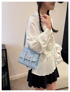 Side view of light blue crossbody bag with silver butterfly buckle on white shirt