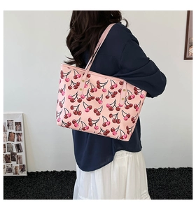 Close-up of pink tote bag with red cherry prints and golden rivets on slim straps
