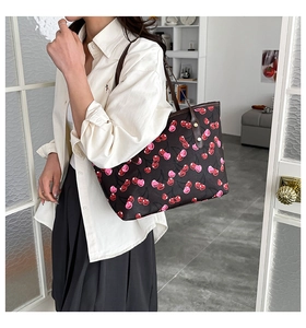 Detail of large tote bag featuring cherry patterns and dark leather shoulder strap