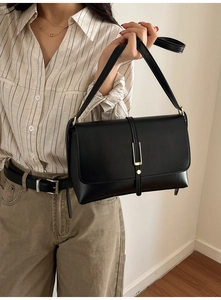 Detail of a minimalist black PU leather shoulder bag with gold clasp shown on a model