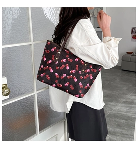 Close-up of cherry print tote bag with brown leather strap and gold rivet details