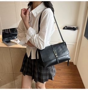 Close-up of black leather crossbody bag with gold metal clasp on a stylish model