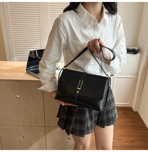Close-up of black leather crossbody bag with vertical gold metal bar and round buckle