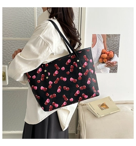 Detailed view of spacious black tote bag with cherry prints worn on shoulder