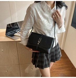 Detailed view of a black leather crossbody bag with gold metal buckle worn by a model