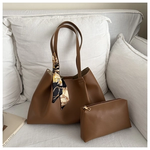 Brown leather tote bag set with a silk scarf detail on a white sofa in a home setting