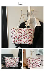Close-up of white tote bag with all-over cherry print and long leather shoulder straps