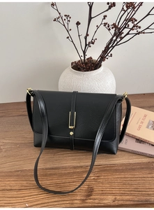 Detail of vintage black faux leather crossbody bag with gold metal buckle on wood table