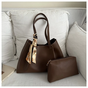 Deep brown leather tote set with printed scarf handle detail on a white sofa