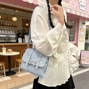 Light blue faux leather crossbody bag with silver bow detail in a stylish street setting