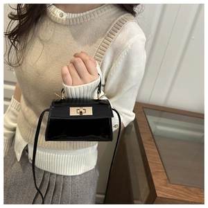 Detail of a mini black patent leather crossbody bag with a gold metal twist lock closure