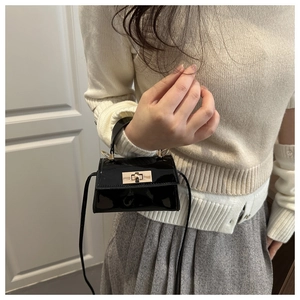 Close-up of black patent leather mini handbag with gold rotary buckle and handle detail
