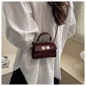 Detail of burgundy patent leather mini crossbody bag with golden metal twist lock and handle