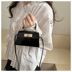 Close-up of black patent leather mini bag with gold twist lock and fine strap detail