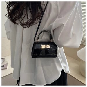 Detail of a black patent leather mini crossbody bag with a gold twist lock on a white shirt
