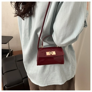 Detail of burgundy patent leather mini crossbody bag with golden metallic lock on model