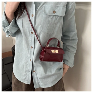 Detail of burgundy patent leather mini crossbody bag featuring a golden turn-lock