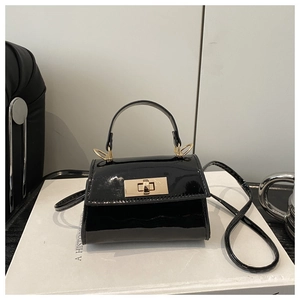 Detail of glossy black patent leather surface and gold twist lock on the mini crossbody bag