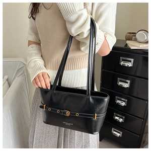 Detail view of a black faux leather tote bag with gold belt buckle and shoulder strap
