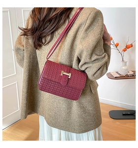 Detail of burgundy woven leather crossbody bag with gold buckle on model in home setting