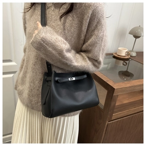 Detalle de un bolso bandolera de cuero negro con cierre de metal giratorio en una modelo