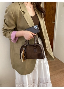 Detail of retro dark brown Boston bag with wooden bead tassel and textured leather finish