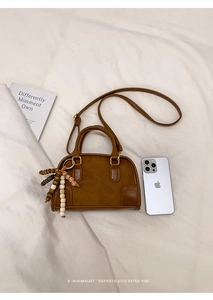 Top view of brown Boston bag with beaded pendant on white pleated fabric background