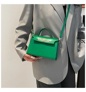 Detail view of a green square handbag with a gold twist lock worn with a grey suit jacket