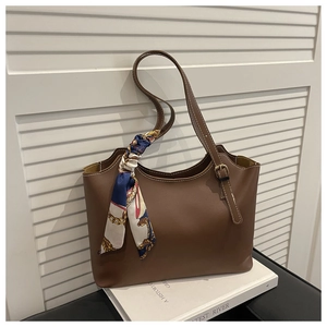 Close-up of caramel leather tote bag with silk scarf on handle and gold buckle
