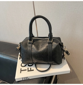 Close-up of black lychee leather handbag with golden hardware and embossed logo