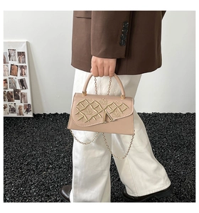 Détail du sac beige en similicuir avec rabat matelassé et bandoulière en chaîne dorée
