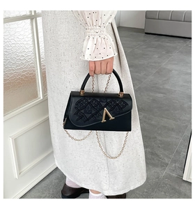 Détail du sac à main en cuir noir avec boucle dorée en V et bandoulière en chaîne