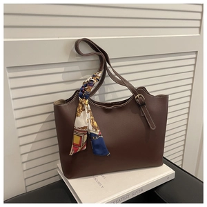 Detail of a brown tote bag with white stitching and a vintage patterned silk scarf
