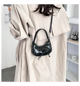 Black crescent hobo bag with bow detail worn crossbody by a model in a beige coat