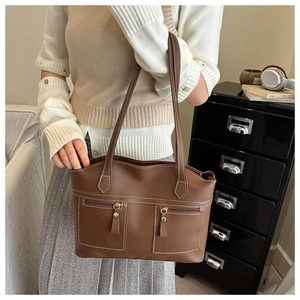 Close-up of brown leather tote bag with dual zipper pockets and white contrast stitching