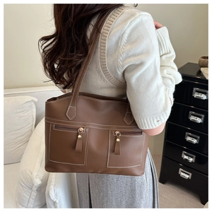 Detail view of brown leather tote bag with white contrast stitching and dual zip pockets