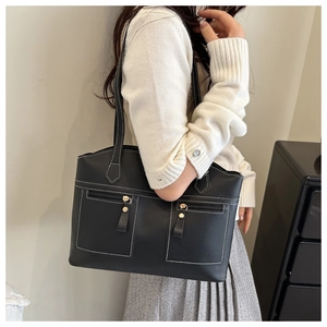 Close-up of black leather tote bag with white contrast stitching and gold zipper pockets