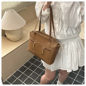 Detailed view of a brown leather tote bag with white contrast stitching and gold zippers