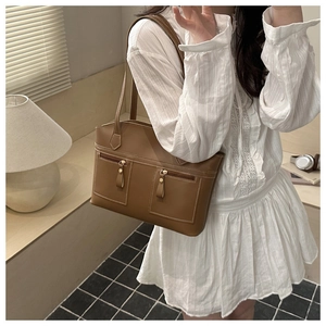 Close-up of brown leather tote bag with dual front zipper pockets and shoulder straps