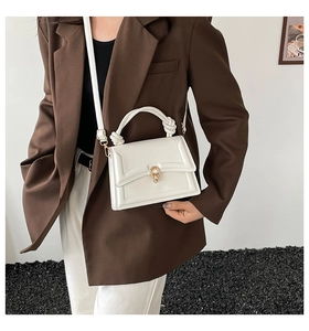 Detail of white leather handbag featuring gold metal buckle and unique knot handle design