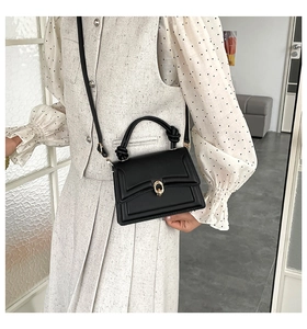 Detail of black leather handbag featuring knotted handle and gold double-ring buckle