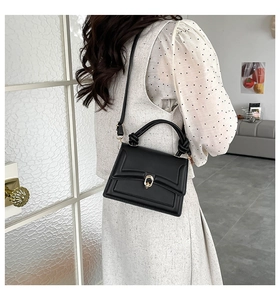Detail view of black leather handbag with golden ring clasp and knotted top handle